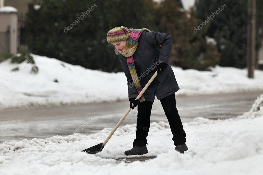 Caucasian woman cleaning snow from sidewalk using shovel, winter time