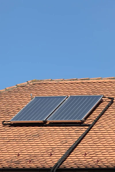 Solar panels at red tiles roof of old house for water heating, with blue sky