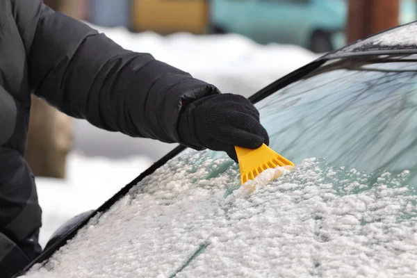 ドライバーの手とツールのスクレーパーのクローズ アップを使用して車のフロント ガラスから雪の清掃 — ストック写真