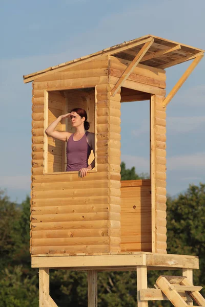 Young female lifeguard observing beach and sea from wooden lifeguard tower