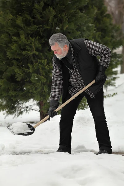 Adult man cleaning snow from sidewalk using shovel, winter time