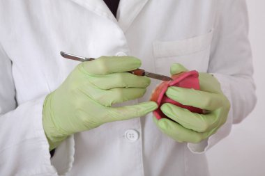 Diş hekimi diş modelleme bıçak, closeup ellerinde eldiven ve aracı kullanarak balmumu protez modeli modelleme