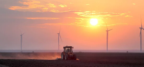Trator no campo e moinhos de vento no nascer ou pôr do sol — Fotografia de Stock