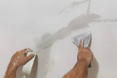 Tavandaki çatlakları onaran işçiler, lifin üzerine alçı serpiştiriyorlar.