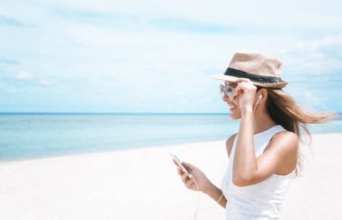 Güzel körfezde arkadaşlarla iletişim kurmak ve müzik dinlemek için telefon ve kulaklık kullanarak yürüyen genç bir kadın.