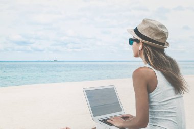 Young woman using laptop computer on a beach. Freelance  concept clipart