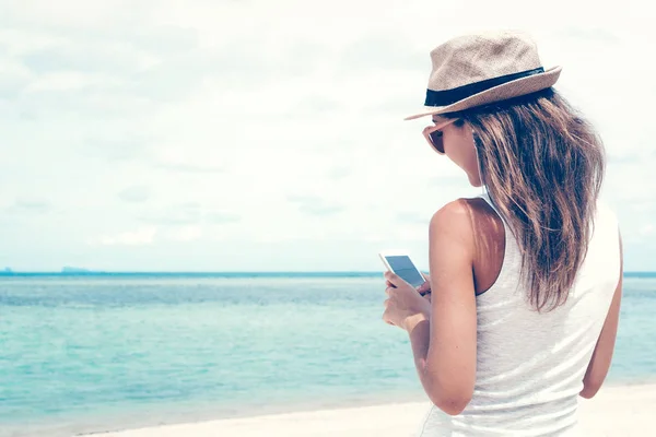 Güzel körfezde arkadaşlarla iletişim kurmak ve müzik dinlemek için telefon ve kulaklık kullanarak yürüyen genç bir kadın.