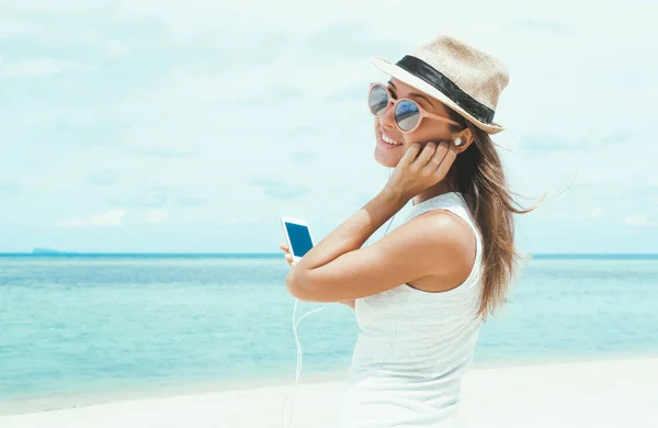 Young woman walking on beautiful bay using phone and headphones for communicate with friends and listening music