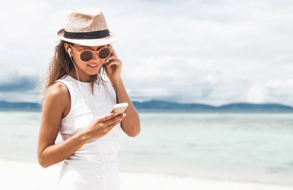 Güzel körfezde arkadaşlarla iletişim kurmak ve müzik dinlemek için telefon ve kulaklık kullanarak yürüyen genç bir kadın.