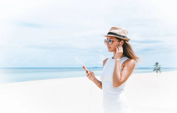 Güzel körfezde arkadaşlarla iletişim kurmak ve müzik dinlemek için telefon ve kulaklık kullanarak yürüyen genç bir kadın.