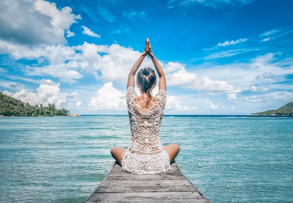 Genç bir kadın sahilde meditasyon yapıyor.