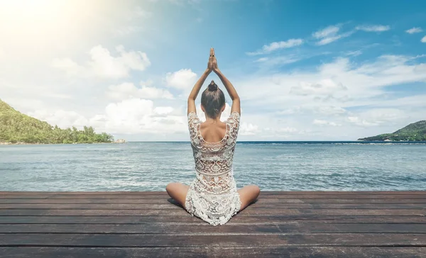 Genç bir kadın sahilde meditasyon yapıyor.