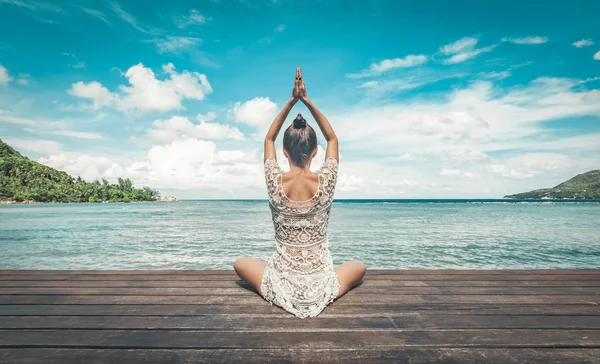 Genç bir kadın sahilde meditasyon yapıyor.