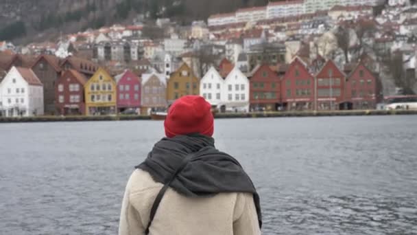 Silhouette of a man in a red hat standing by the water, colorful houses in the background 50 fps — Stock Video