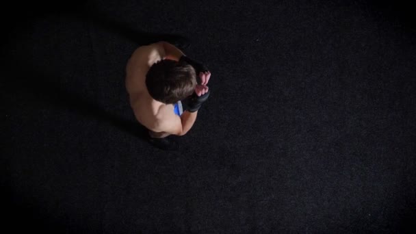 Joven boxeador topless caucásico haciendo calentamiento, golpeando, boxeo, tiro superior, fondo negro. 50 fps — Vídeo de stock