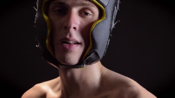 Retrato de un joven boxeador caucásico en topless y cansado, con casco de boxeo, protector de cabeza, mirando a la cámara, fondo negro 50 fps — Vídeo de stock