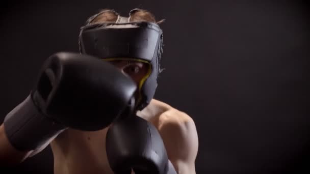 Giovane boxer caucasico in topless boxe, jabs, girando da parte, casco protettivo, sfondo nero, guarda la fotocamera 50 fps — Video Stock