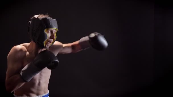 Young caucasian topless boxer boxing, jabs, protective helmet, black background, side view 50 fps — Stock Video