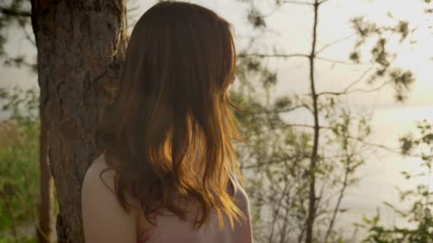 Joven chica jengibre hermosa en la playa en el bosque de pie cerca del árbol, la naturaleza, la silueta, mirando a la cámara 50 fps — Vídeo de stock