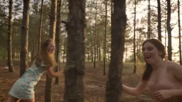 Две молодые кавказские девушки в платьях бегают по лесу, играют в мяч, валяют дурака, природа на заднем плане — стоковое видео