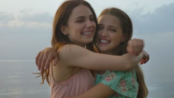 Twee jonge Kaukasische meisjes in jurken knuffelen op lake, lachen, glimlachen, natuur in de achtergrond, camera kijken — Stockvideo