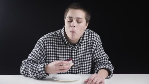 Jovem garota incomum está comendo bolo de queijo, lambendo os dedos, concepção de dieta, fundo preto — Vídeo de Stock