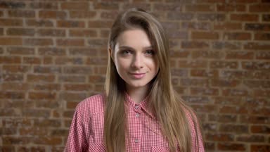 Genç güzel kız smilimg, kameraya, tuğla arka plan izliyor