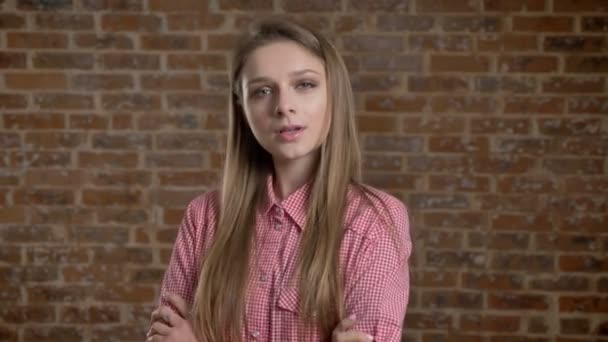 Young beautiful confident girl with arms crossed, watching at camera, brick background — Stock Video