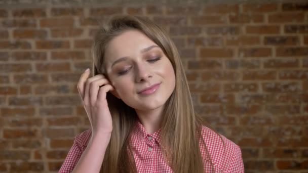 Young confident girl touches her hair, watching at camera, brick background — Stock Video