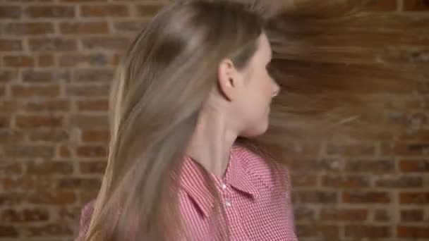 若い魅力的な女の子彼女の頭の動きは、彼女の髪、煉瓦背景を果たしています。 — ストック動画