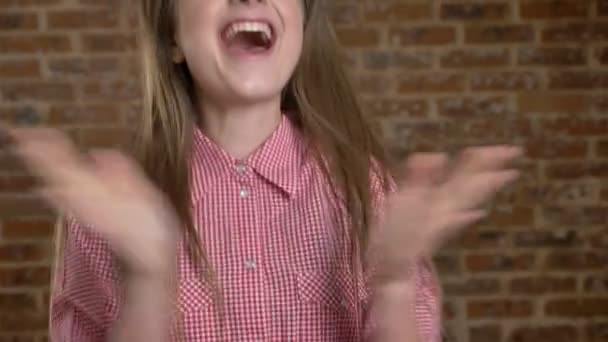 Young pretty girl jumps, claps her hands, cries from happiness, watching at camera, brick background — Stock Video