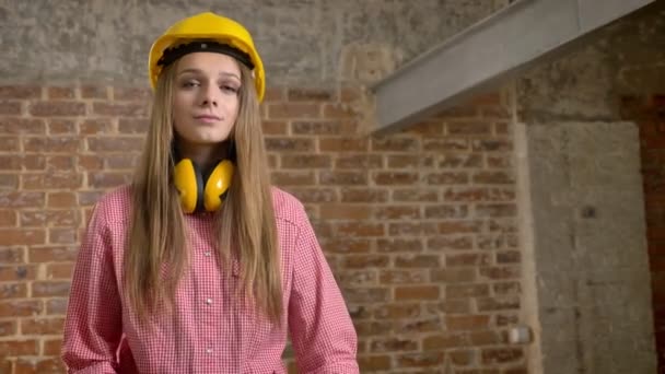Young confident girl builder is crossing arms, nodding her head, watching at camera, brick background — Stock Video