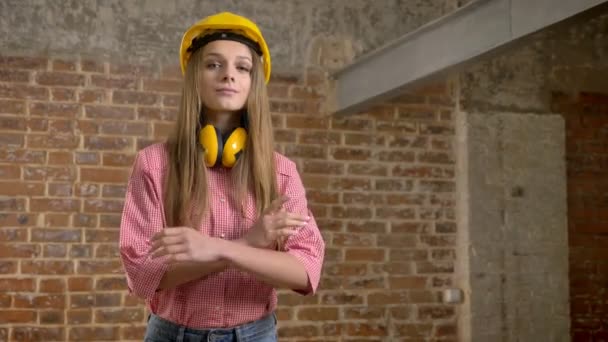 Joven constructor de chica confiada está cruzando los brazos, levantando la ceja, asintiendo con la cabeza, mirando a la cámara, fondo de ladrillo — Vídeos de Stock