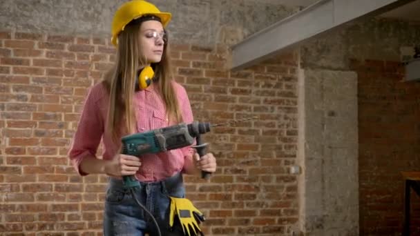 Junge ernsthafte Bauarbeiterin hält Bohrer in den Händen, dreht sich an, baut eine Konzeption — Stockvideo