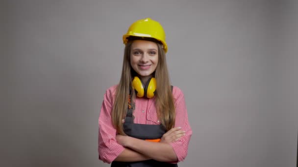 Young pretty girl builder is crossing arms, smiling, watching at camera, grey background. — Stock Video