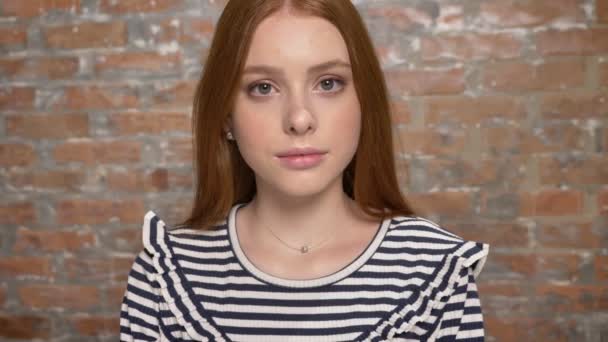 Retrato de una linda chica adolescente brillante mirando a la cámara, pared de ladrillo en el fondo — Vídeo de stock