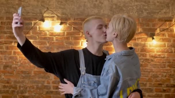 Junges attraktives Hipsterpaar macht Selfie auf Smartphone, küsst, albert herum, Kommunikationskonzept, Backsteinhintergrund — Stockvideo