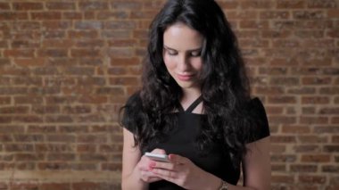 Genç güzel esmer kız surs Internet onun smartphone, gülümseyen, iletişim kavramı, tuğla backgroung