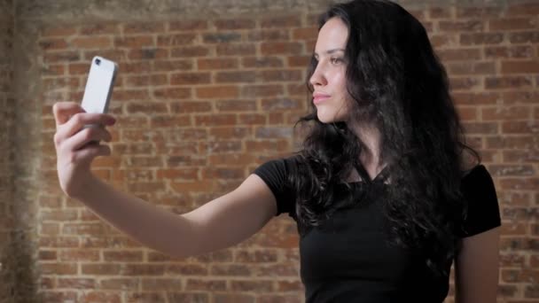 Genç güzel esmer kız onun Smartphone'da, poz, iletişim anlayışı, tuğla arka plan selfie yapıyor — Stok video