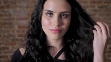 Genç çekici kız saçını, kamera, flört anlayışı, tuğla arka plan, izlerken dokunur