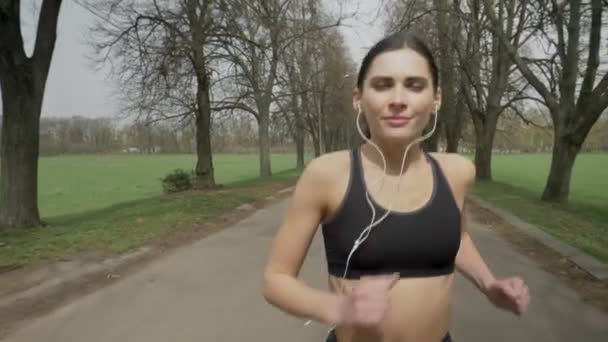 Chica del deporte joven se ejecuta con auriculares en el parque en verano, estilo de vida saludable, concepción del deporte — Vídeo de stock