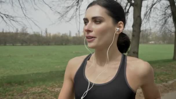 Jovem menina esporte feliz está correndo com fones de ouvido no parque no verão, estilo de vida saudável, concepção de esporte, vista lateral — Vídeo de Stock