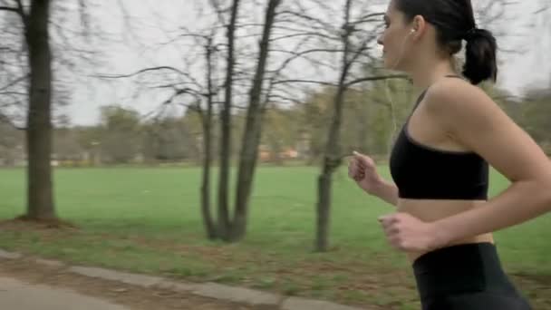 Young sport meisje draait met koptelefoon in park in zomer, gezonde levensstijl en sport conceptie, camera ronde bewegen — Stockvideo