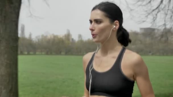 Young passen meisje is joggen in het park in de zomer, luisteren naar muziek, gezonde levensstijl, sport conceptie, zijkant — Stockvideo