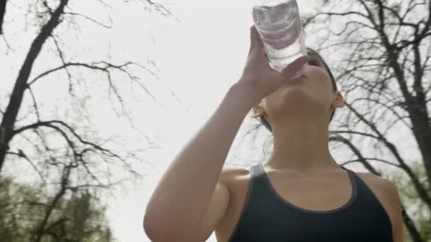 フィット若い女の子は、夏、健康的なライフ スタイル、スポーツ観に公園で水を飲む、底面、丸いカメラ移動 — ストック動画