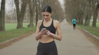 Uygun genç kız parkta çalıştıran yaz, iletişim anlayışı, spor anlayışı onun smartphone, izlerken