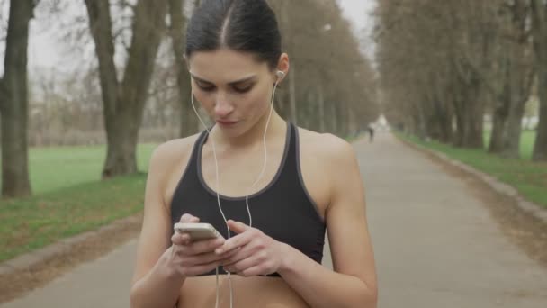 Young fsport girl is turning on music on her smartphone, running, healthy lifestyle, sport conception — Stock Video