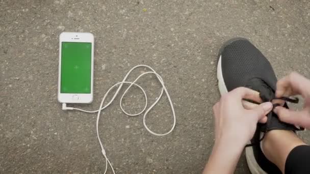 Meisje sportman bindt haar schoenveters terwijl haar smartphone en oortelefoons zijn tot op de grond, chroma scherm, communicatieconcept — Stockvideo