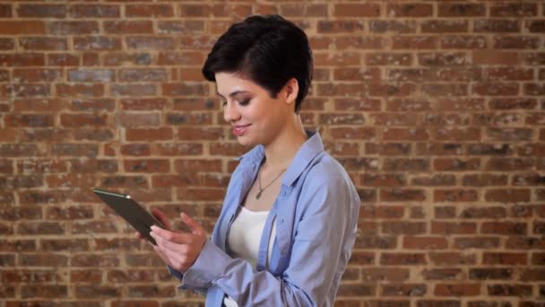 Menina bonita jovem está digitando mensagem em seu tablet, conceito de comunicação, fundo de tijolo — Vídeo de Stock