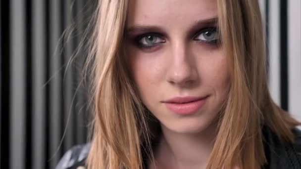 Jonge mooie vrouwen met zware make-up in zwarte jas op zoek in de camera en bijten haar lip, striped muur achtergrond — Stockvideo
